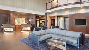 A spacious lobby with a large sectional sofa, a reception desk, and a kitchen area. - Courtyard by Marriott Waterloo St. Jacobs (Township of Woolwich)