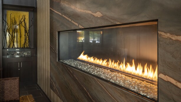 A modern interior with a glass-fronted fireplace, dark wood paneling, and a decorative wall piece. - Courtyard by Marriott Waterloo St. Jacobs (Township of Woolwich)