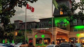 A Courtyard Marriott hotel with a traditional architectural style, featuring a central entrance with arched windows and a flagpole with a Canadian flag. - Courtyard by Marriott Waterloo St. Jacobs (Township of Woolwich)