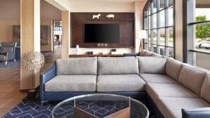 A modern living room with a sectional sofa, a flat-screen TV, and a large window offering a view of the street. - Courtyard by Marriott Waterloo St. Jacobs (Township of Woolwich)
