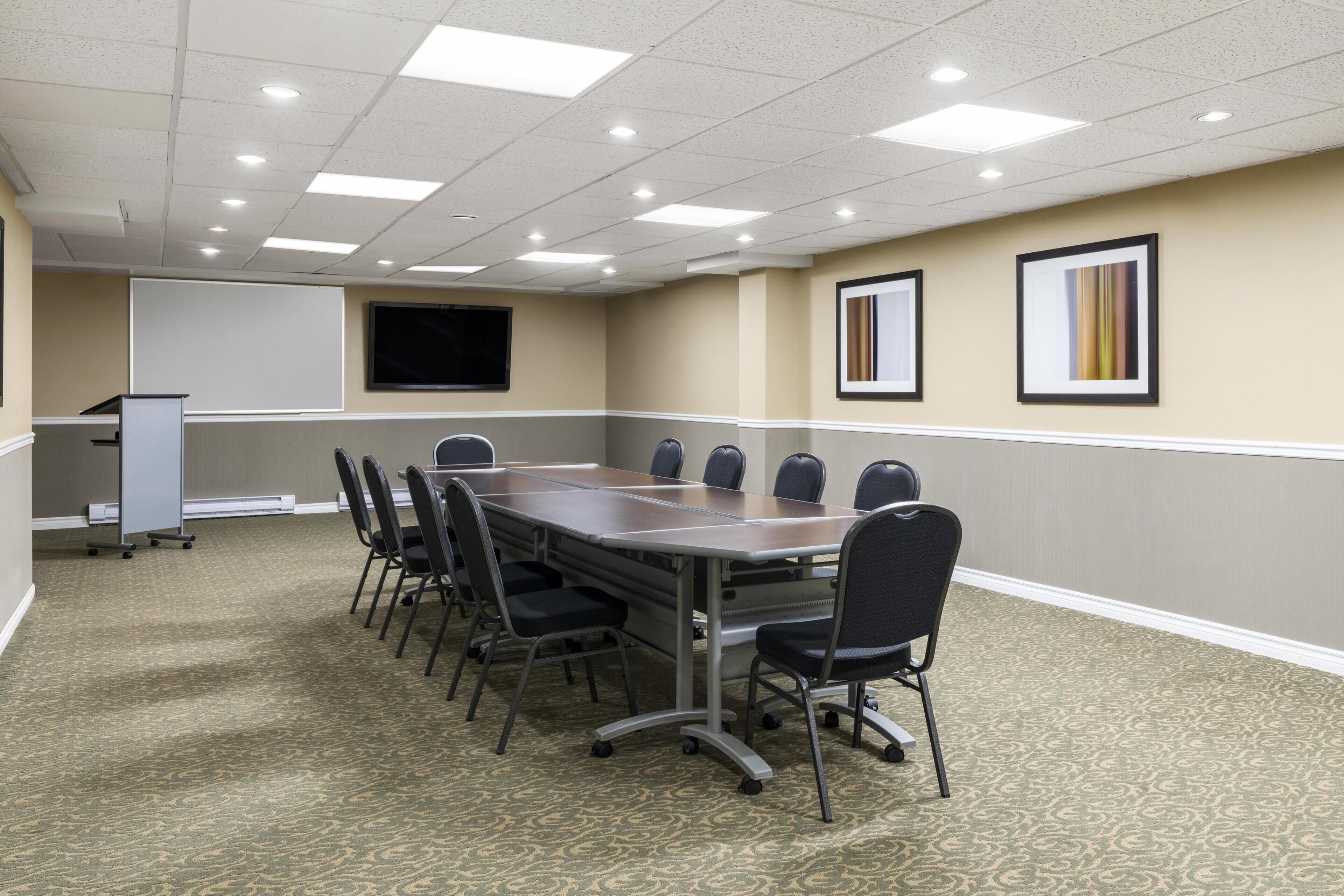 Uma sala de conferências com uma mesa comprida, cadeiras, tela de projetor e quadros nas paredes.