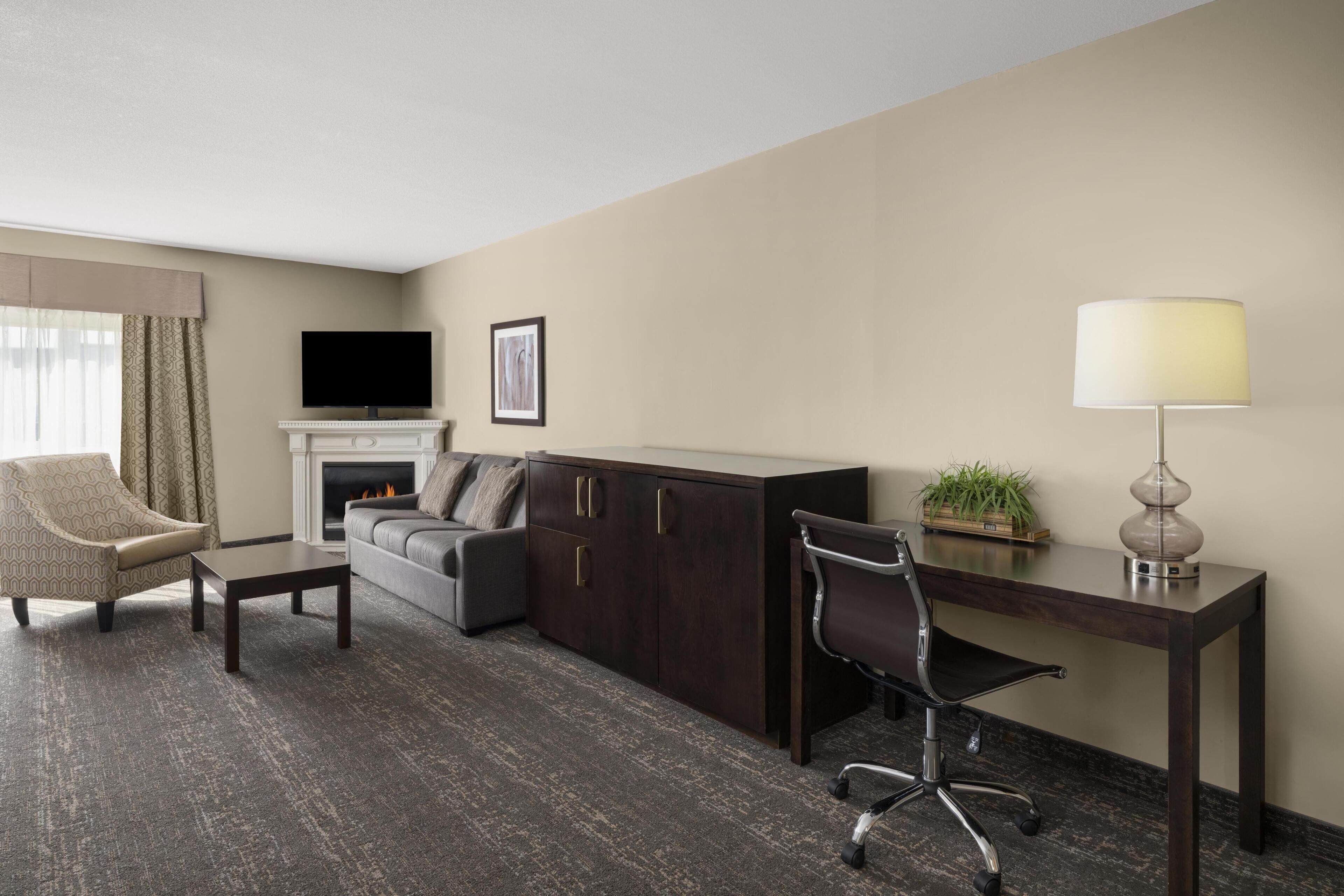 A hotel room with a sofa, armchair, desk, and a television.