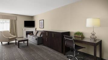 A hotel room with a sofa, armchair, desk, and a television.