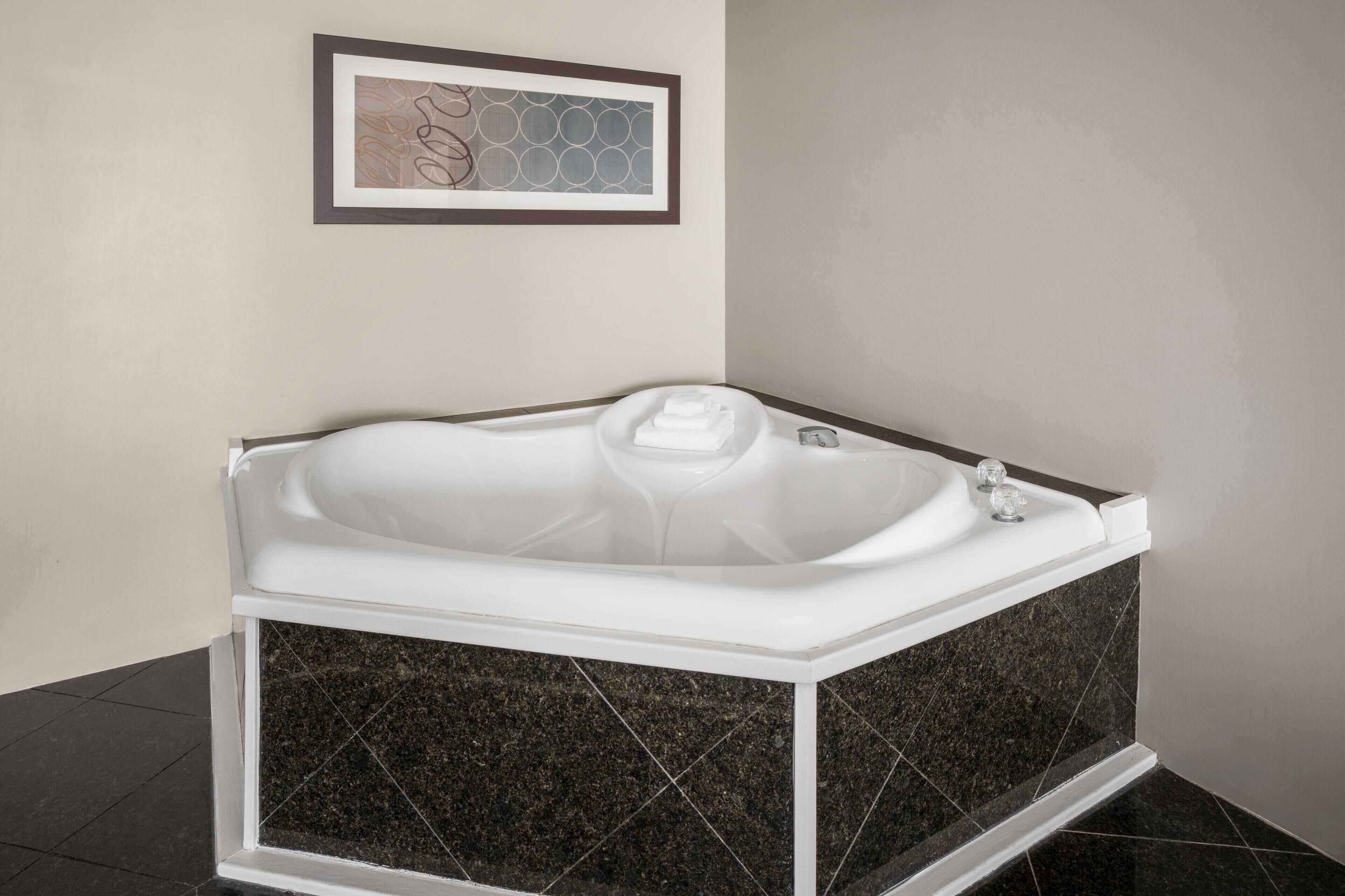 A modern bathroom with a freestanding bathtub, dark marble tiles, and a framed abstract artwork on the wall.