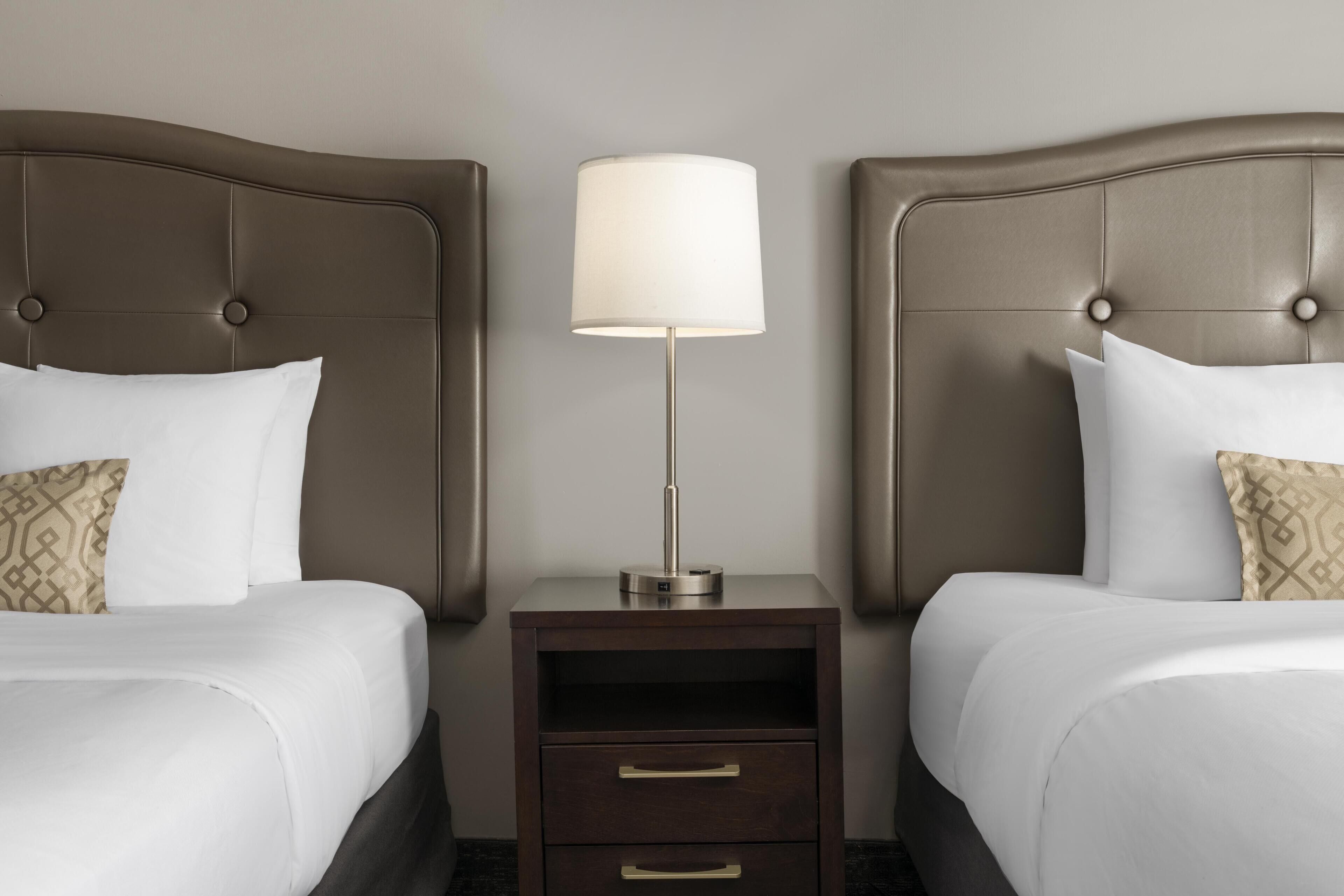 Een hotelkamer met twee bedden, een nachtkastje met een lamp en een ladekast.