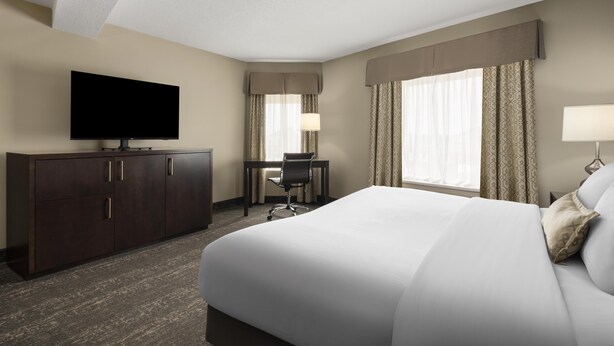 A hotel room with a bed, a desk, a television, and a window with curtains. - Best Western Swan Castle Inn (Cochrane)