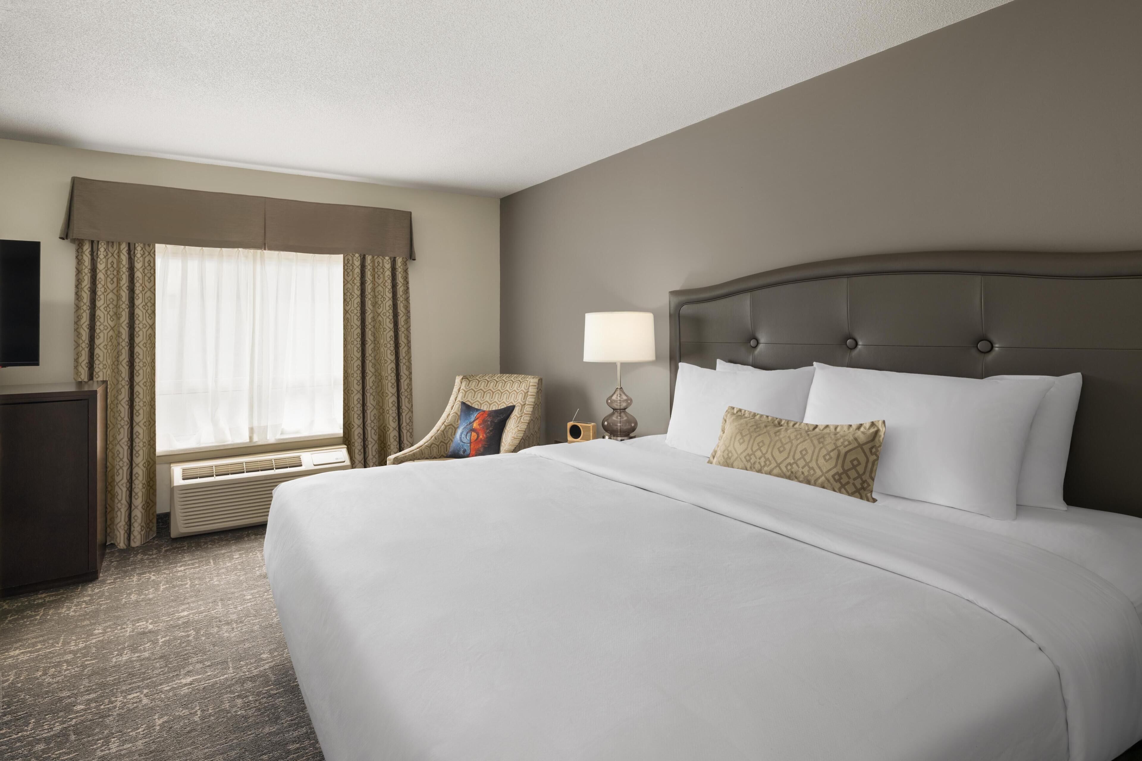 A hotel room with a large bed, a chair, a desk, a lamp, and a television.