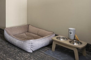 A pet bed and feeding station with a checkered pattern and a metal bowl.