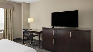 A hotel room with a bed, a desk with a chair, a television on a cabinet, and a lamp.