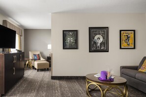 A modern living room with a flat-screen TV, a sofa, a chair, and a coffee table. There are three framed posters on the wall. - Best Western Swan Castle Inn (Cochrane)