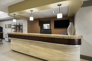 A reception desk with a marble top, overhead lighting, a flat-screen TV, and a decorative vase.