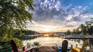 Vista del lago con barcos amarrados, un atardecer y sillas Adirondack.