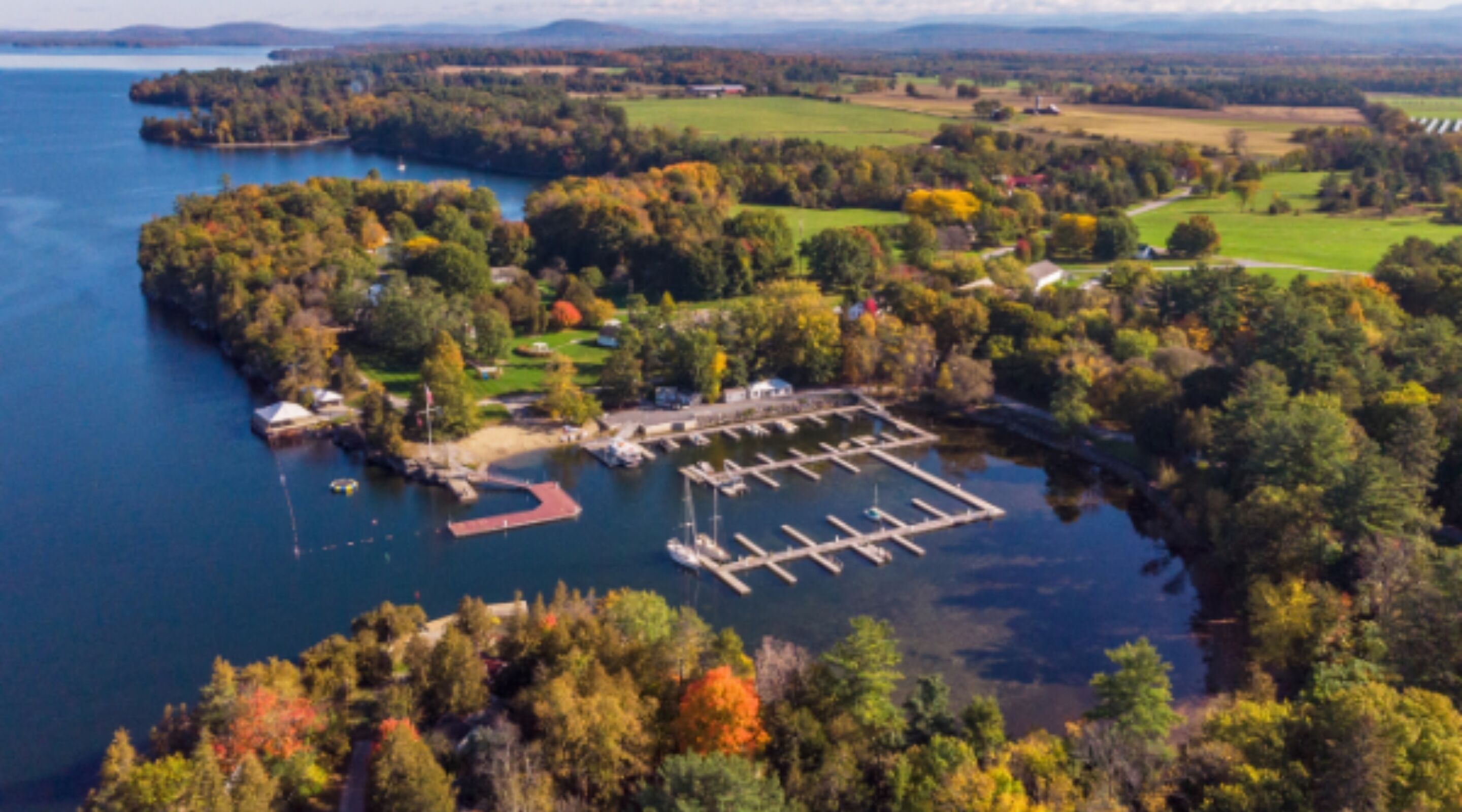 An aerial view of a lakeside property with a dock, marina, and surrounding forested area.