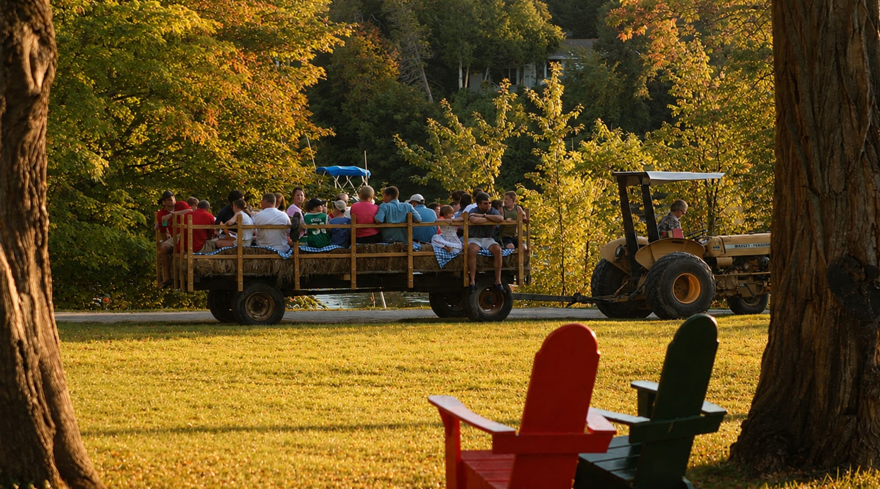 A group of people on a wooden wagon with a tractor in a park with trees and grass.