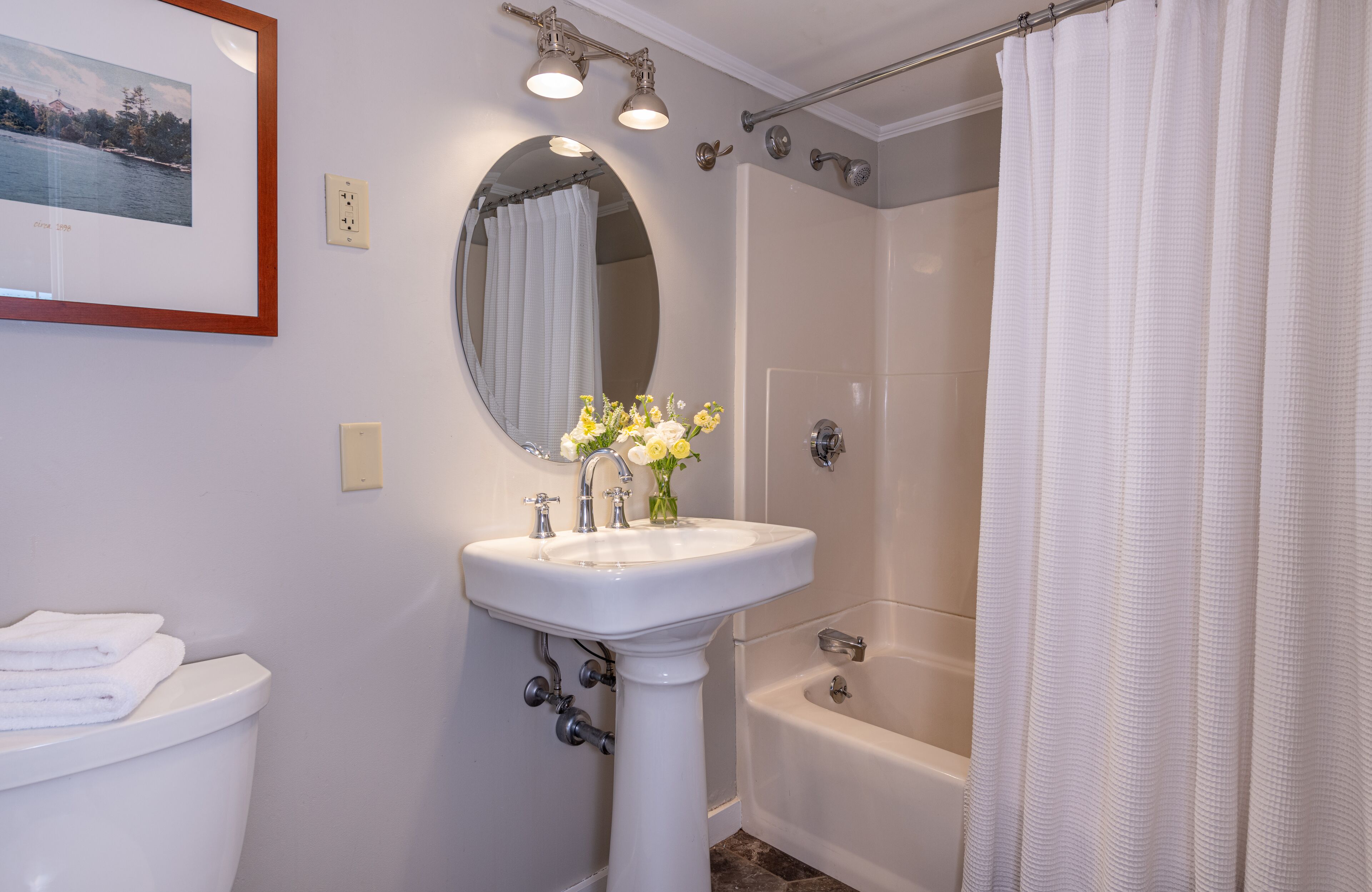 A bathroom with a pedestal sink, a mirror, a framed photograph, a shower curtain, and a bathtub.