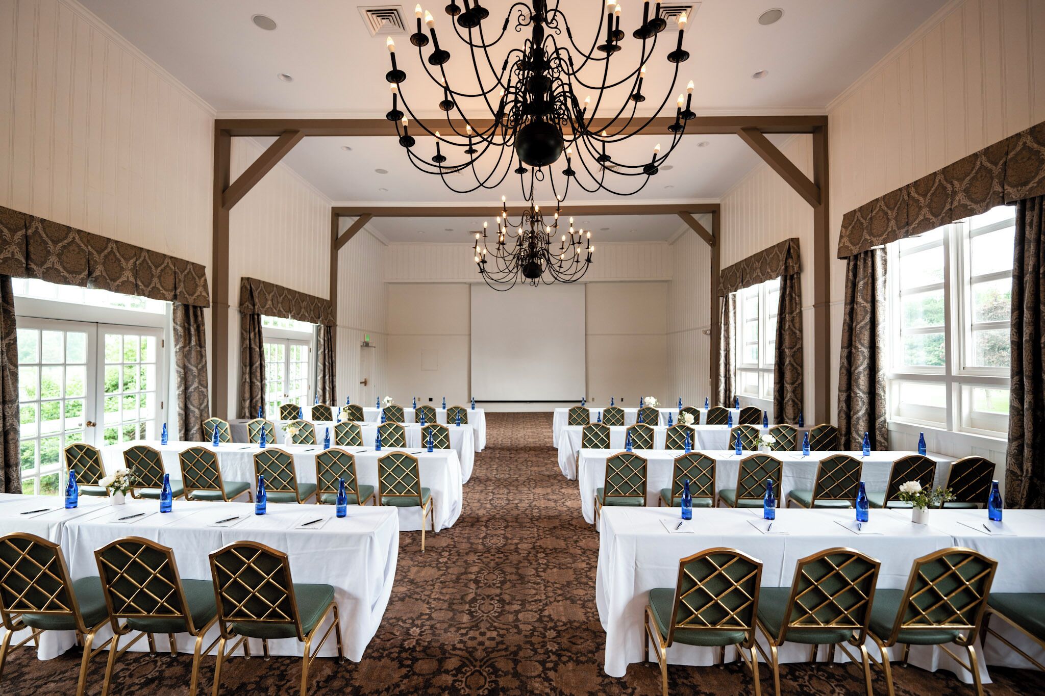 A conference room with multiple tables and chairs, a chandelier, and large windows.