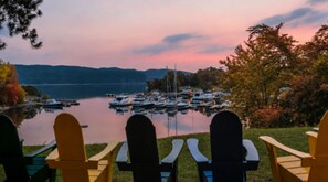 Vista de un lago con barcos amarrados, sillas orientadas al agua y un atardecer sereno.