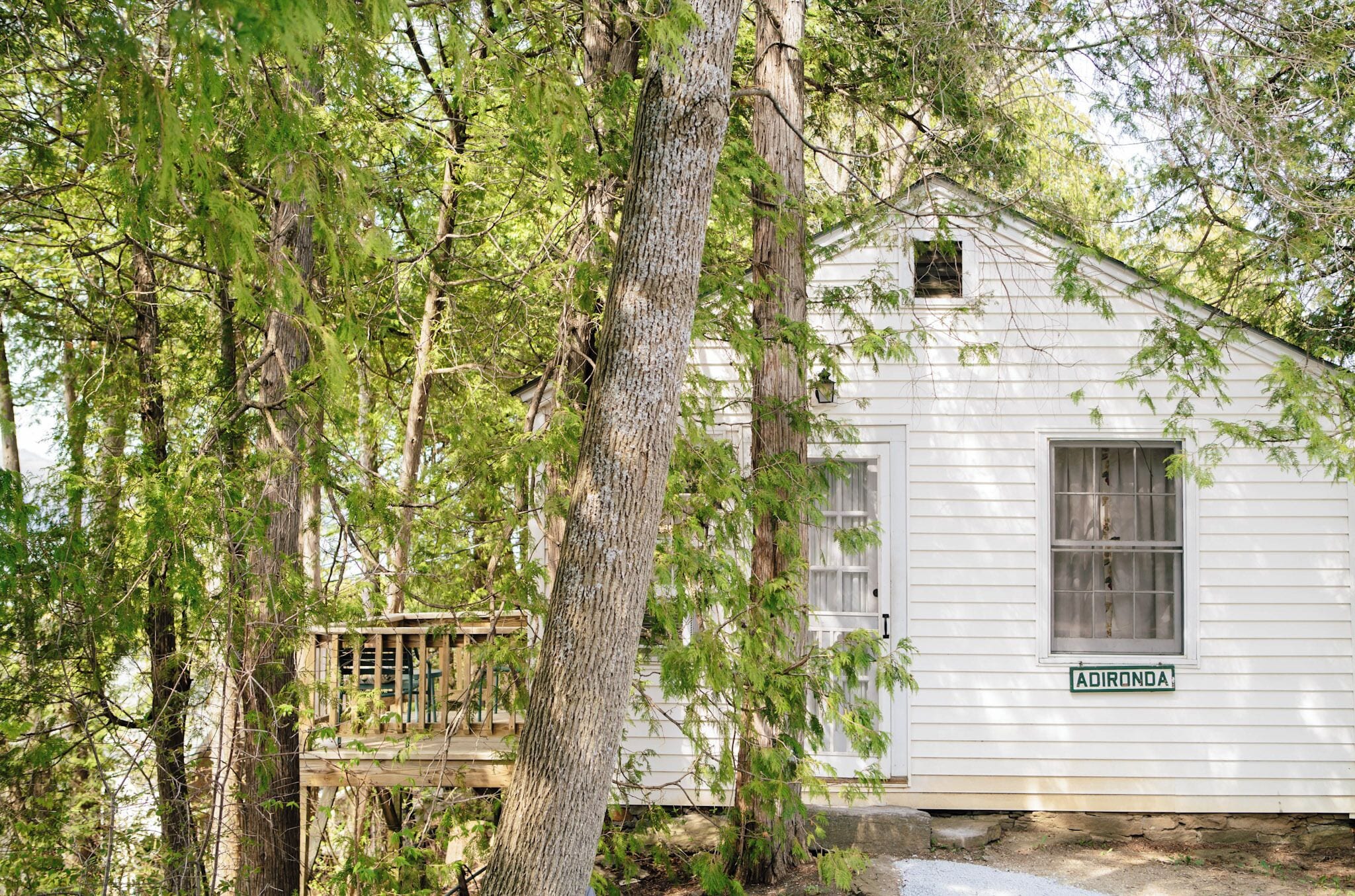 A white wooden cabin with a small deck, surrounded by trees.