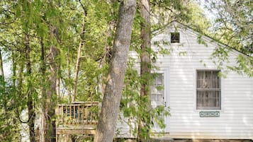 A white wooden cabin with a small deck, surrounded by trees.