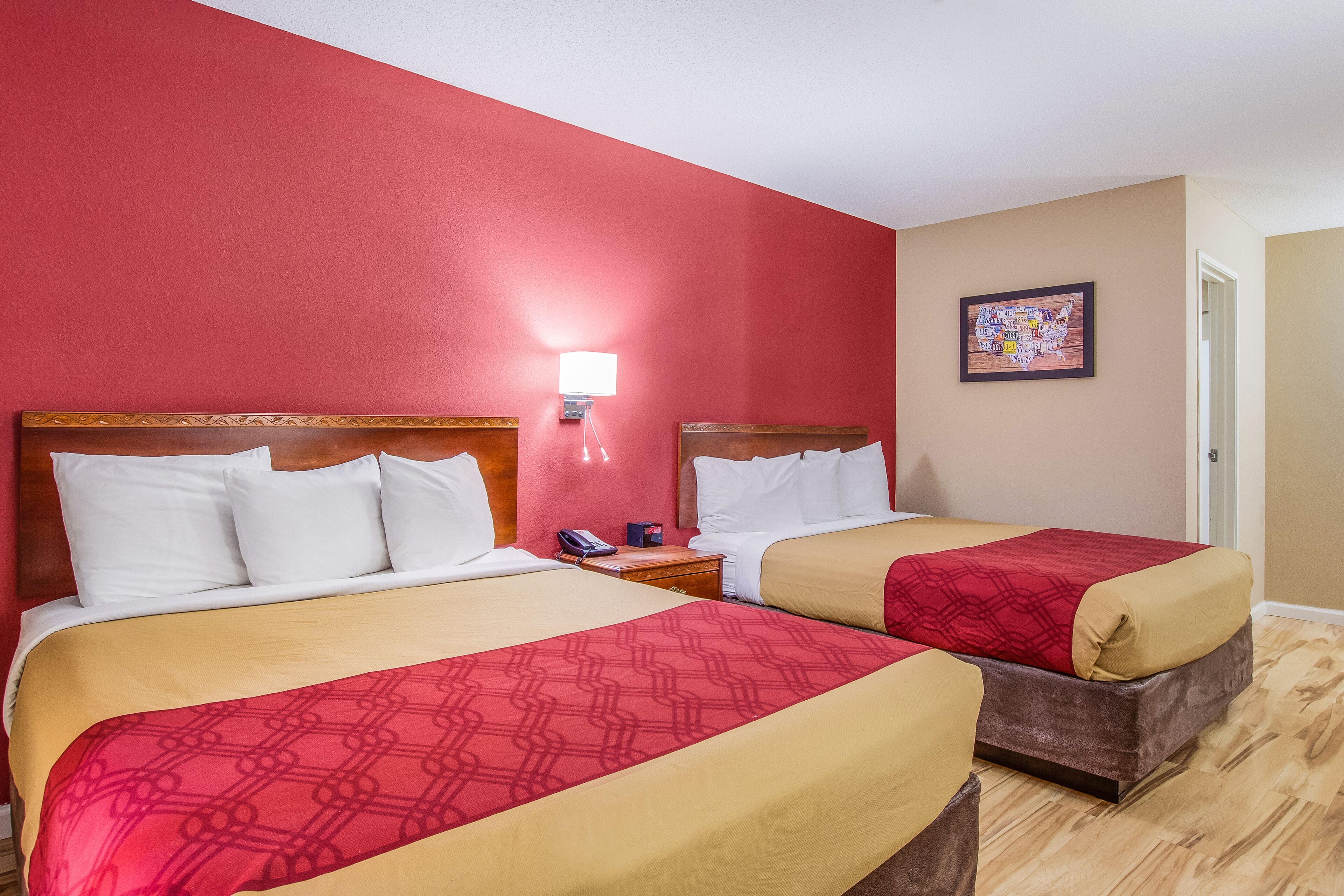 Ein Hotelzimmer mit zwei Betten, einem Nachttisch, einer Lampe und einer gerahmten Karte an der Wand.