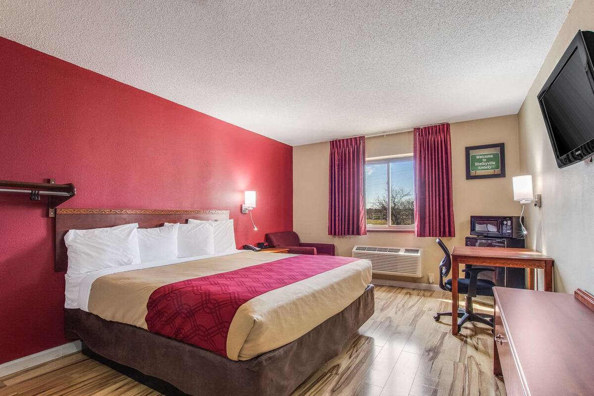 Een hotelkamer met een bed, een bureau, een stoel, een televisietoestel en een raam met gordijnen.
