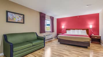 Een hotelkamer met een groene bank, een bed met een rode accentmuur en een kaart aan de muur.