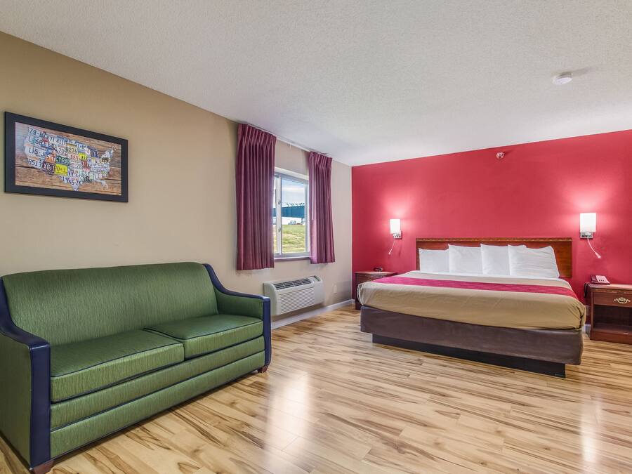 A hotel room with a green sofa, a bed with a red accent wall, and a map on the wall.