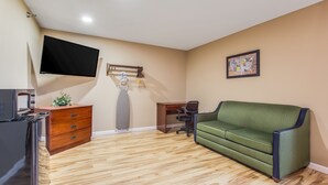 Una habitación con piso de madera, un sofá verde, un escritorio, una silla, un aparador, un televisor de pantalla plana y un mapa en la pared.