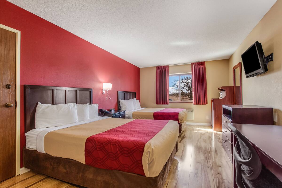 Een hotelkamer met twee bedden, een bureau, een televisie en een raam met gordijnen.
