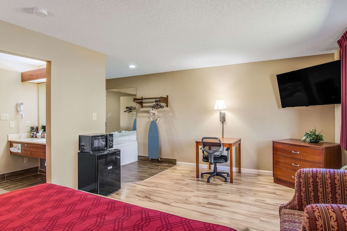 Een hotelkamer met kitchenette, bureau met stoel, televisie, bed en gestreept fauteuil.