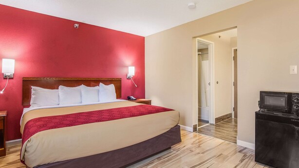 Una habitación de hotel con una cama grande, paredes rojas, piso de madera, televisor y microondas.