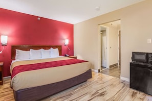 A hotel room with a large bed, red walls, a wooden floor, a TV, and a microwave.