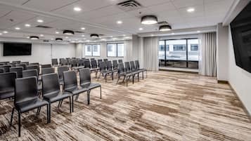 A conference room with rows of black chairs, a large screen, and large windows with curtains.