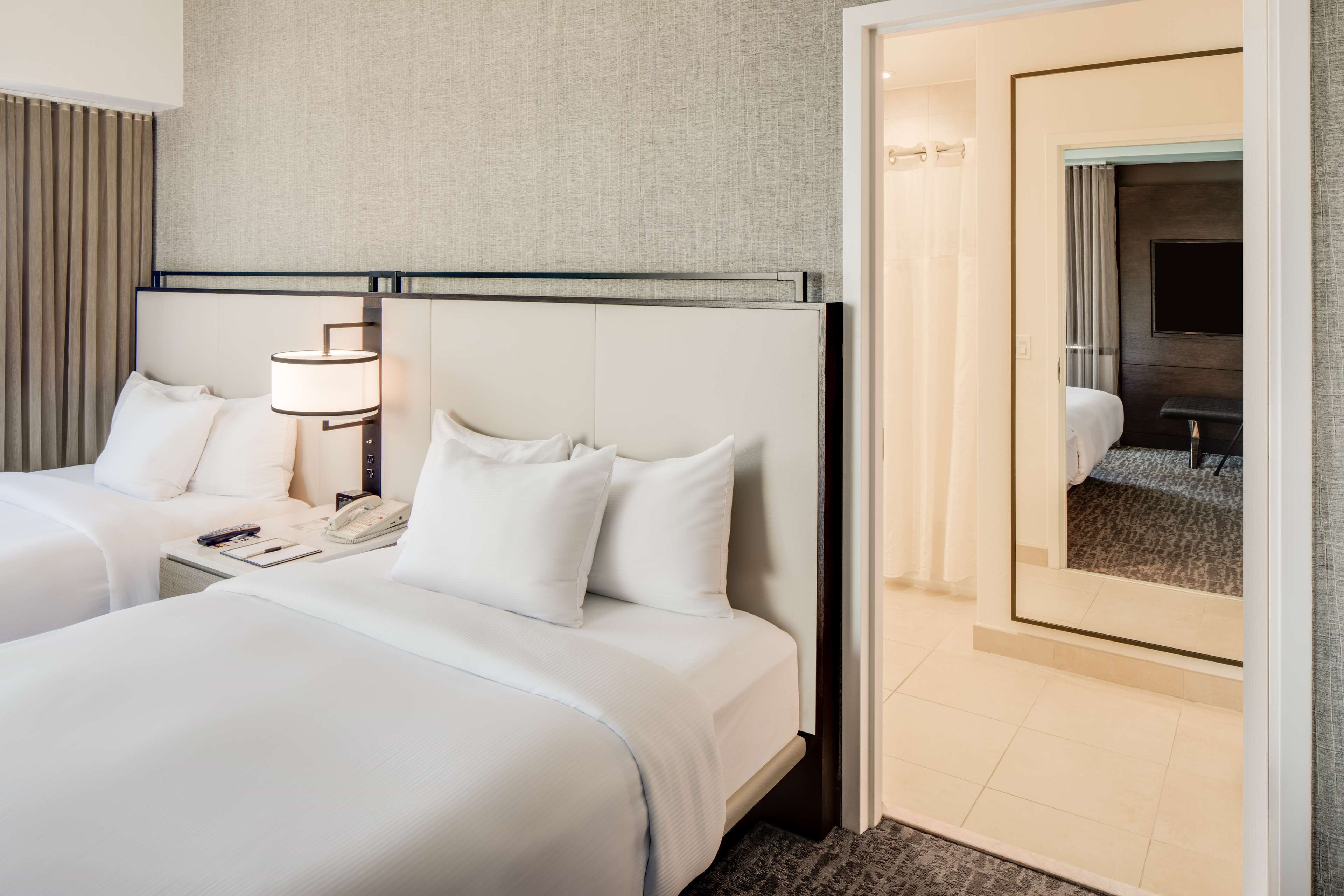 Une chambre d’hôtel avec deux lits, une table de chevet avec une lampe, un téléphone et un miroir.