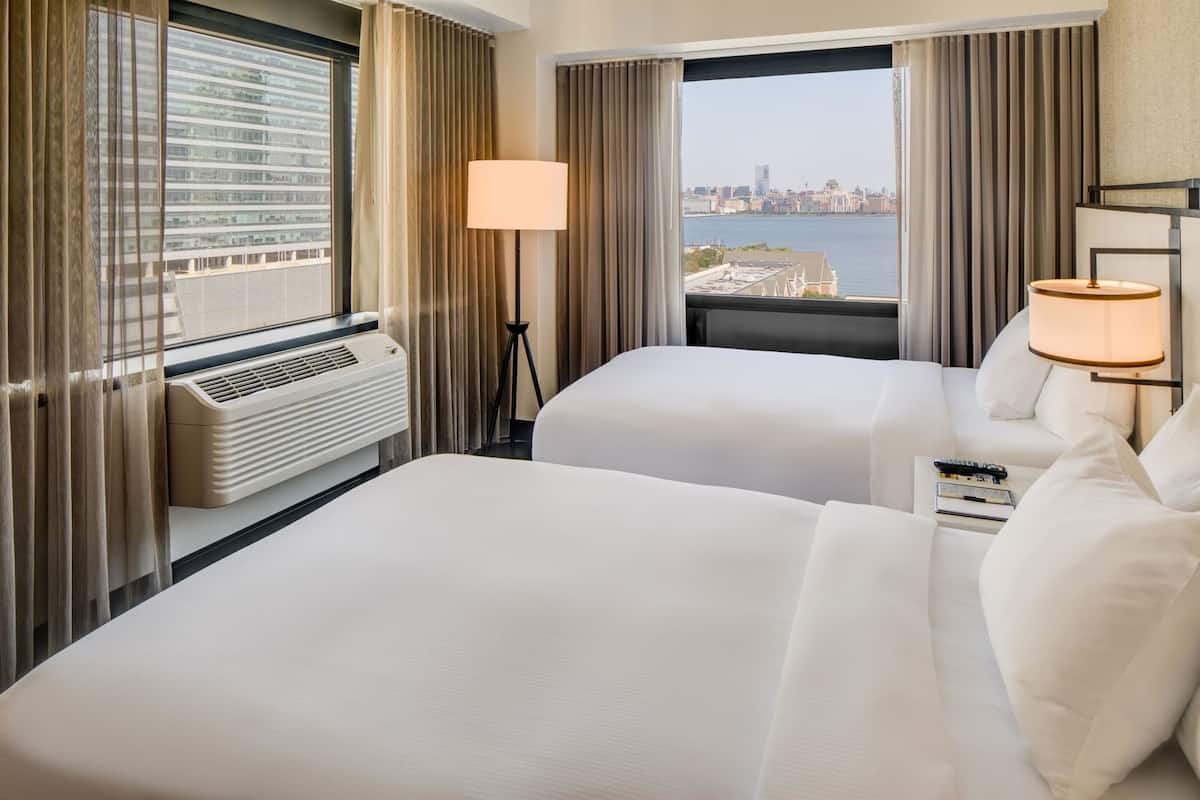 A hotel room with two beds, a view of a cityscape, and a window with curtains.