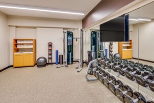Un gimnasio con equipo de ejercicio, un espejo grande y estantes de almacenamiento.