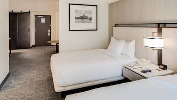 A hotel room with two beds, a framed picture on the wall, a bedside table with a lamp, and a door leading to another room.