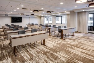 Un salón de conferencias con varias mesas y sillas, amplias ventanas con cortinas y un diseño de techo moderno.