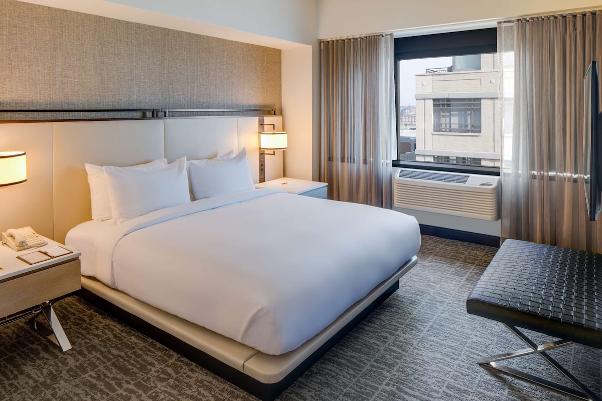 A hotel room with a large bed, bedside lamps, a desk with a phone, and a window with curtains.