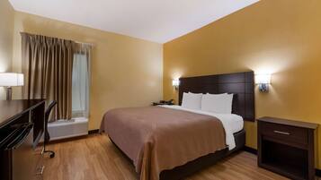 A hotel room with a bed, bedside table, lamp, and a desk with a chair.