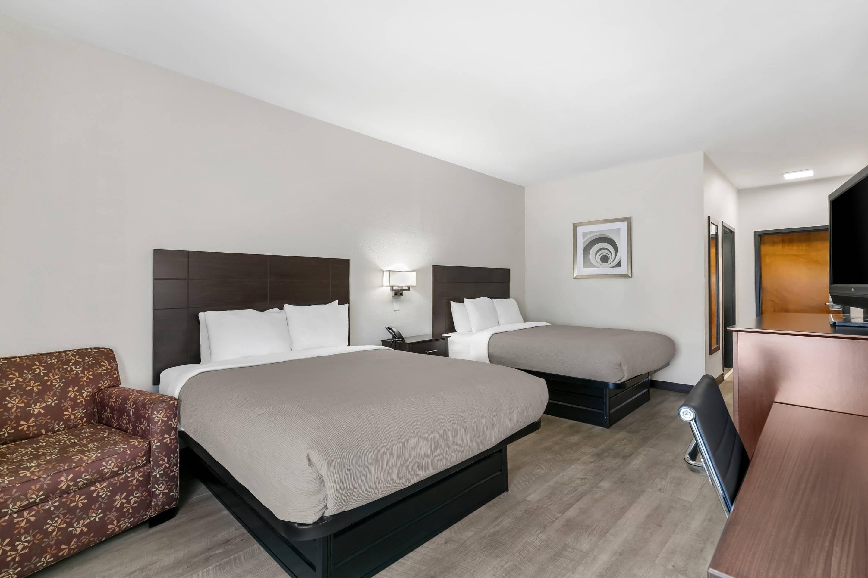 Habitación de hotel con dos camas, un sofá, un escritorio y un cuadro en la pared.