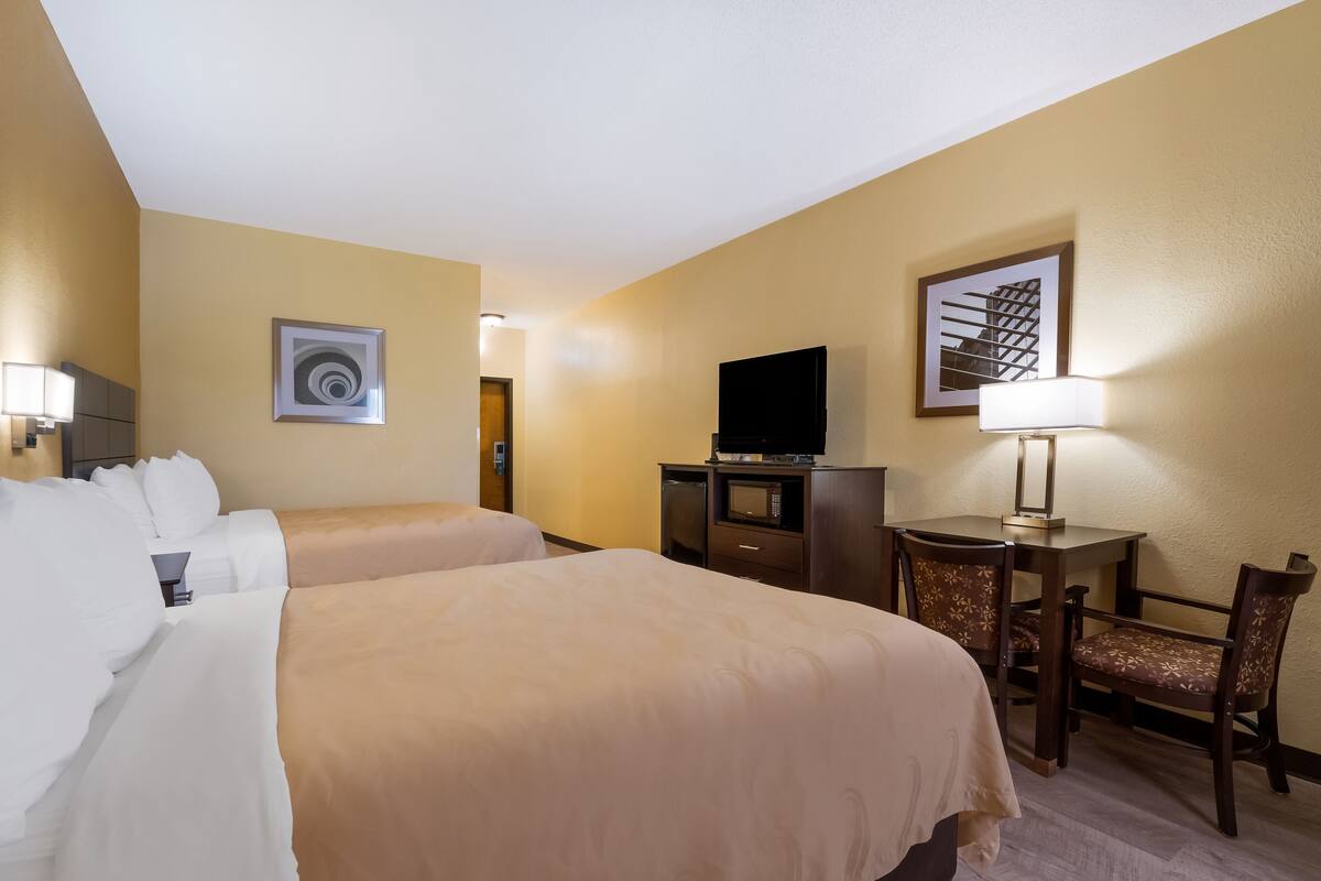 A hotel room with two beds, a desk with a chair, a television, and artwork on the walls.