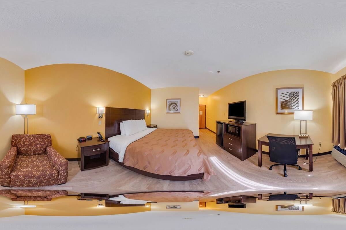A hotel room with a bed, a desk, a chair, a TV, and a window with curtains.