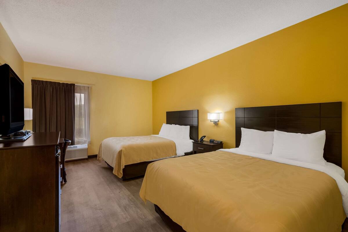 A hotel room with two beds, a desk, a TV, and a window with curtains.