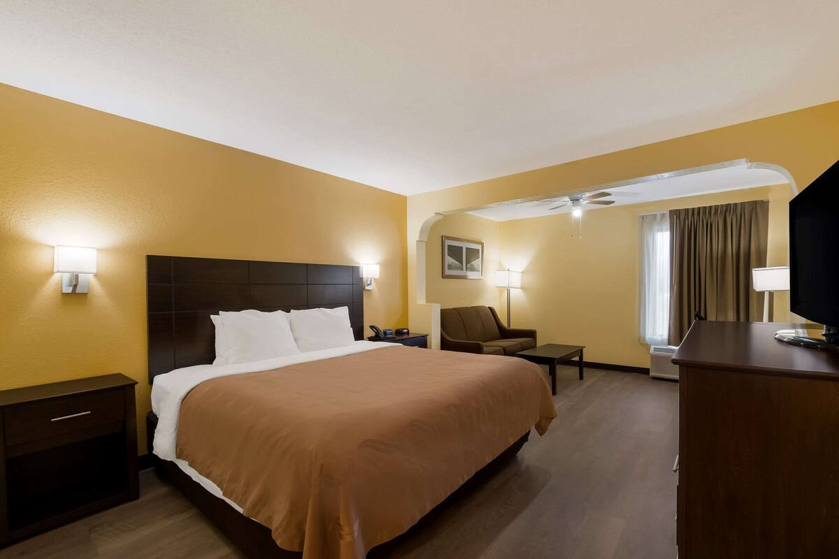 A hotel room with a large bed, bedside tables, a chair, a desk, and a television.