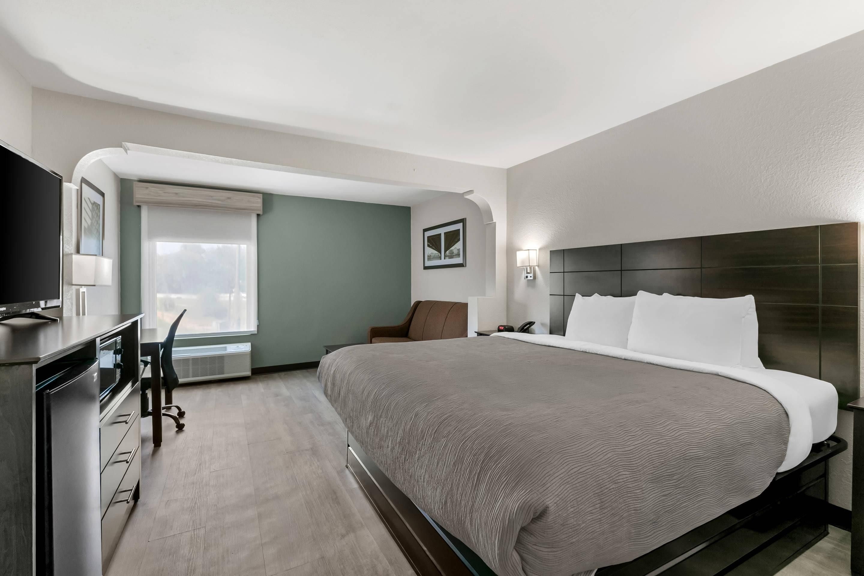 A hotel room with a bed, a desk, a chair, a TV, and a window.