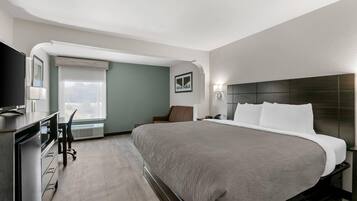 A hotel room with a bed, a desk, a chair, a TV, and a window.