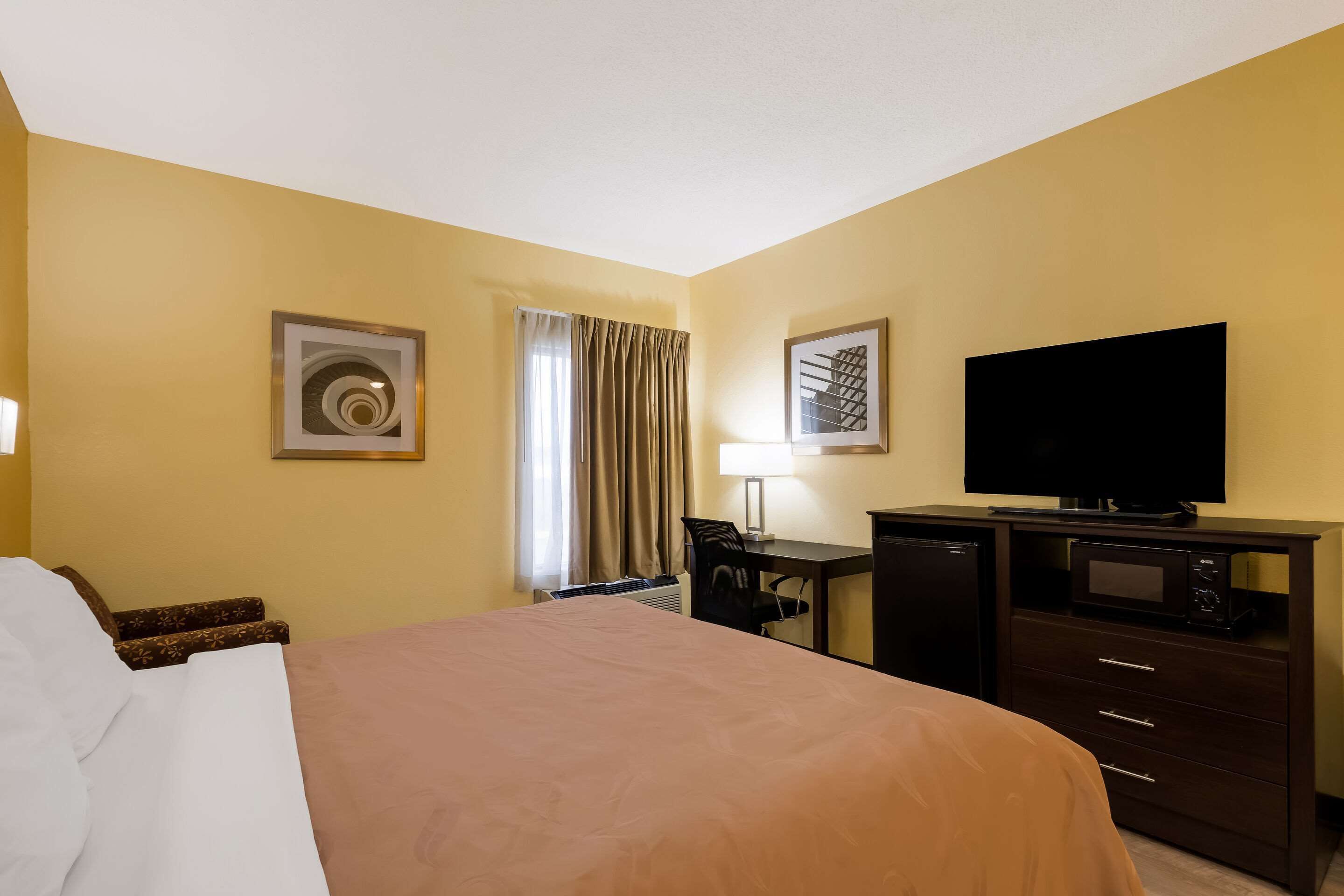 A hotel room with a bed, a desk, a television, and a microwave.
