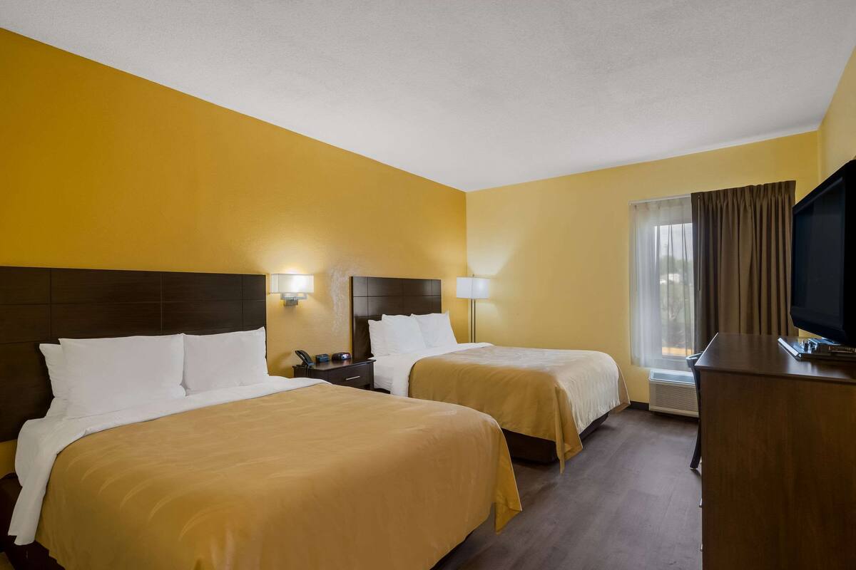 A hotel room with two beds, a TV, a desk, and a window with curtains.
