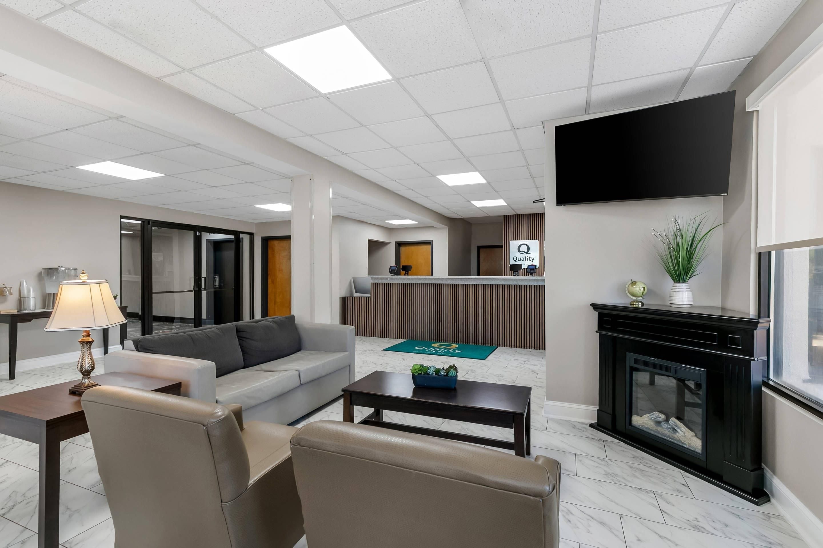 A hotel lobby with a sofa, armchair, coffee table, fireplace, television, reception desk, and a reception area.